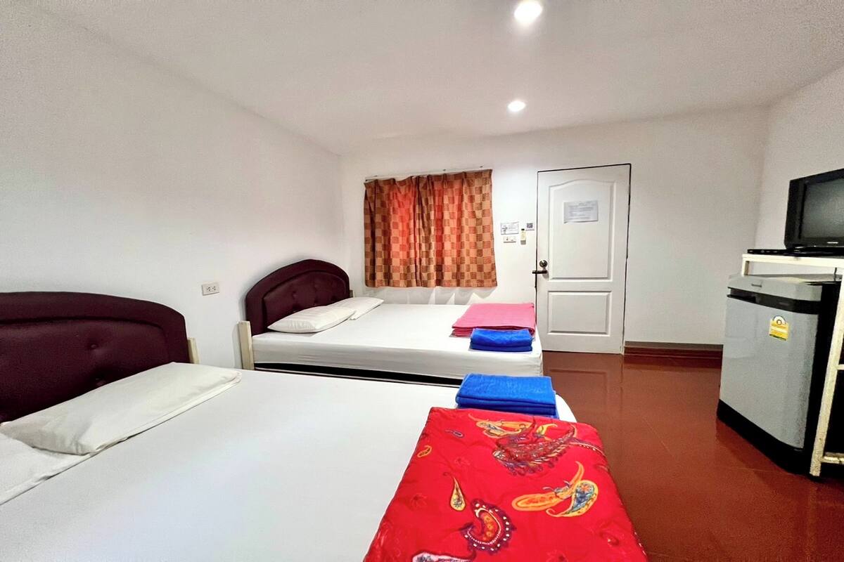 Ein Zimmer mit zwei Betten, einem Schreibtisch mit Fernseher, einer Tür und einem Fenster mit Vorhängen.