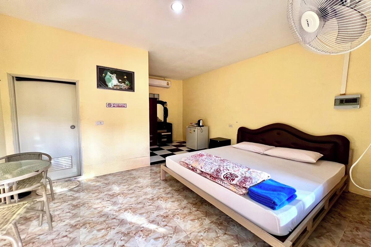 Ein Zimmer mit einem Bett, einem Schreibtisch, einem Stuhl, einem Ventilator und einer Tür.