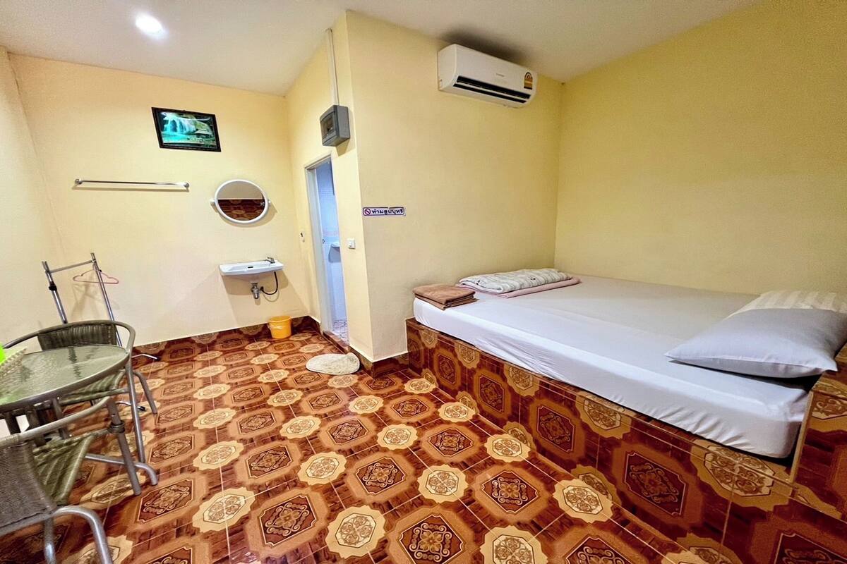 Ein kleines Zimmer mit einem Bett, einem Waschbecken, einem Spiegel und einem Stuhl.