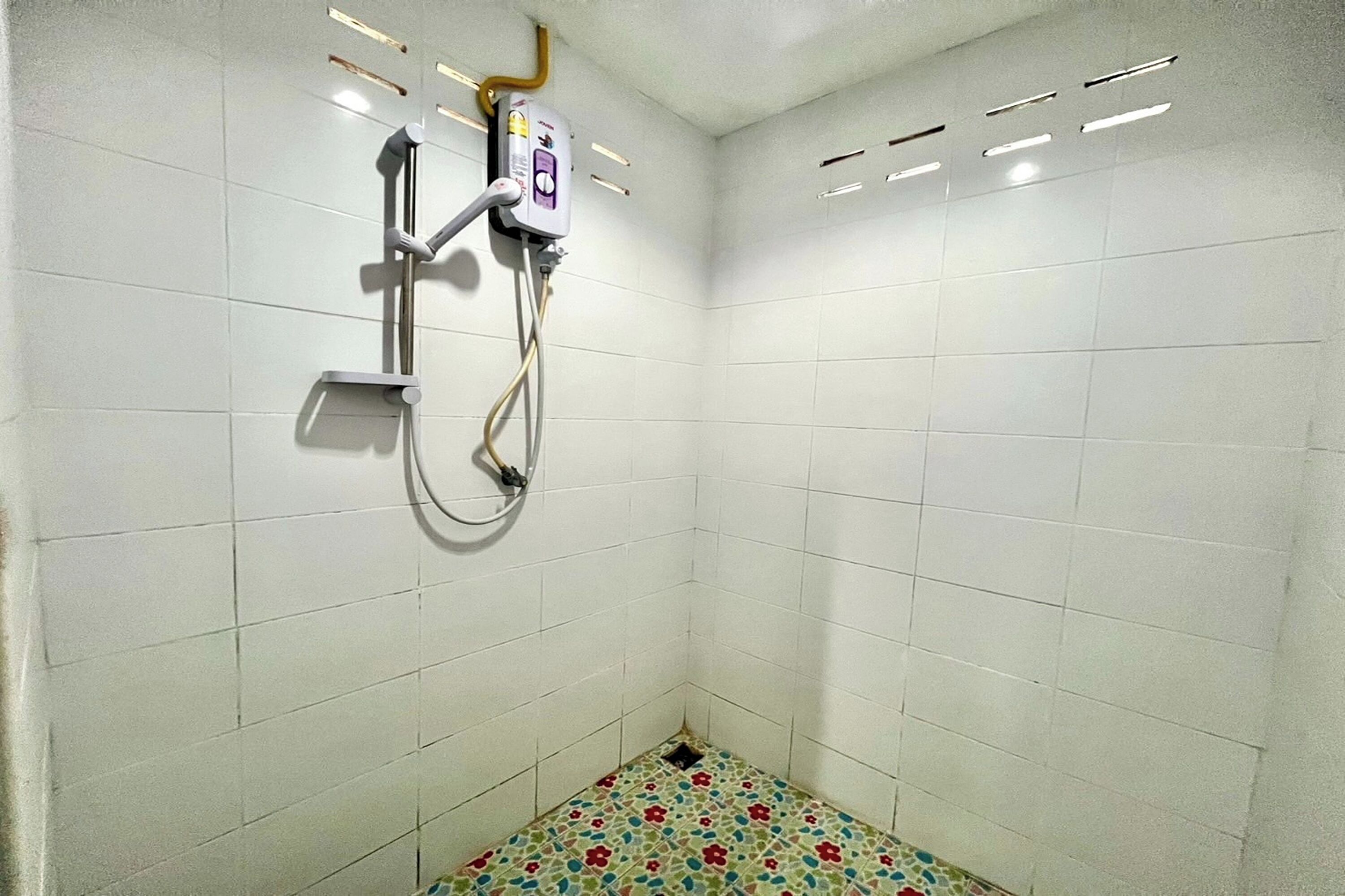 A small, tiled shower area with a showerhead and control panel.