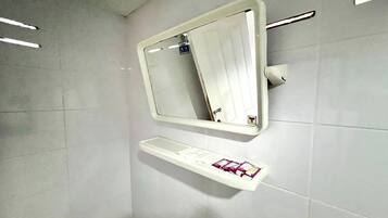 A bathroom with a white tiled wall, a mirror, and a shelf with toiletries.