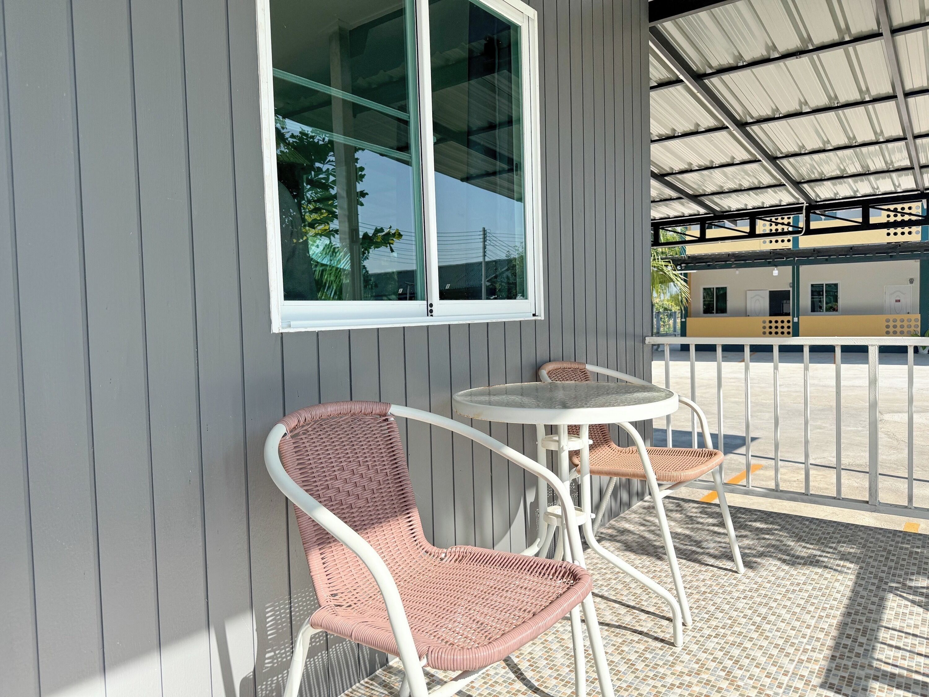 Un espace extérieur aménagé avec des meubles de jardin en osier, une table, une fenêtre et, au fond, un bâtiment doté d’un toit en métal.