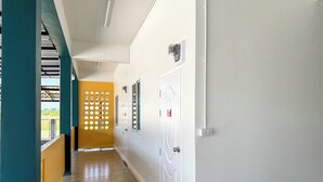 A corridor with a wooden floor, white walls, and a yellow partition with circular cutouts. - Jira Hotel (Lampang)