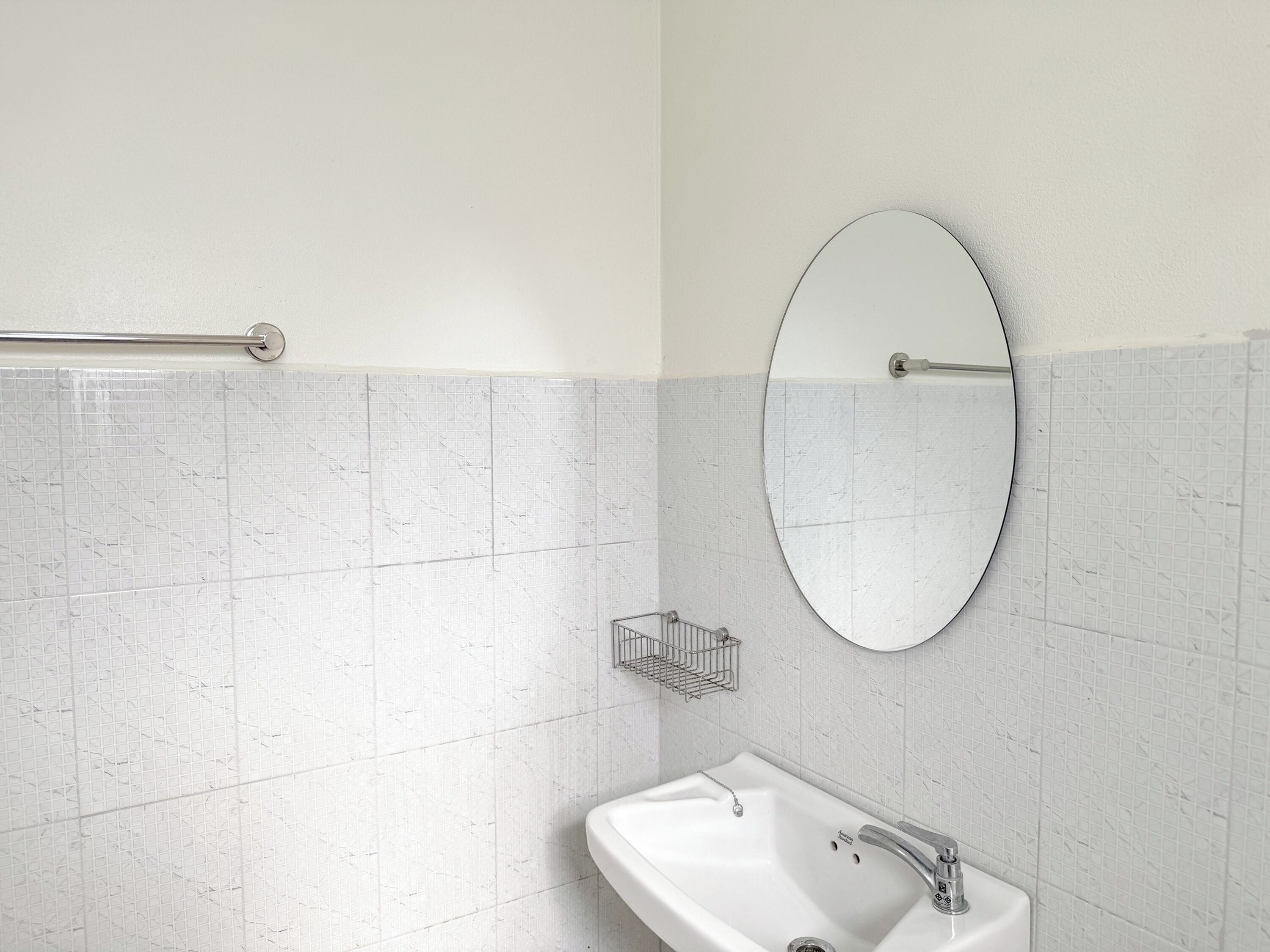 A bathroom with a white sink, a round mirror, and a towel rack.