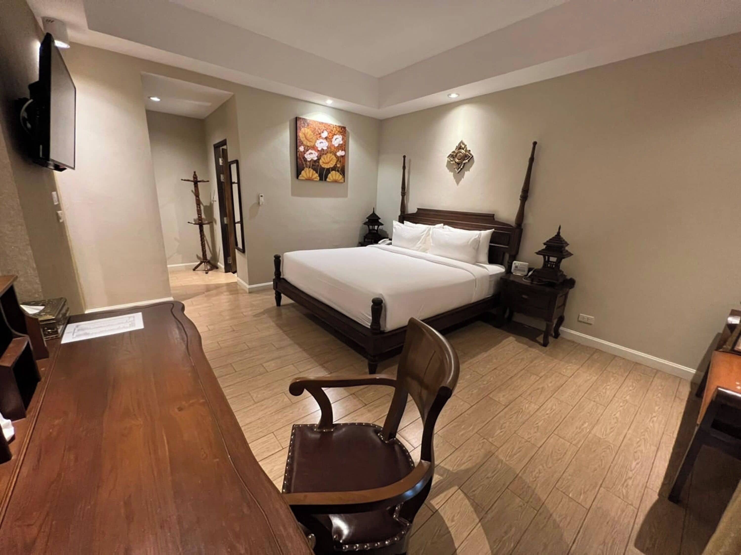 A hotel room with a large bed, a wooden desk, a chair, and a painting on the wall.