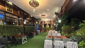 An outdoor restaurant with tables and chairs, surrounded by greenery and decorative lighting. - Kokhaburi Hotel (Ko Kha)