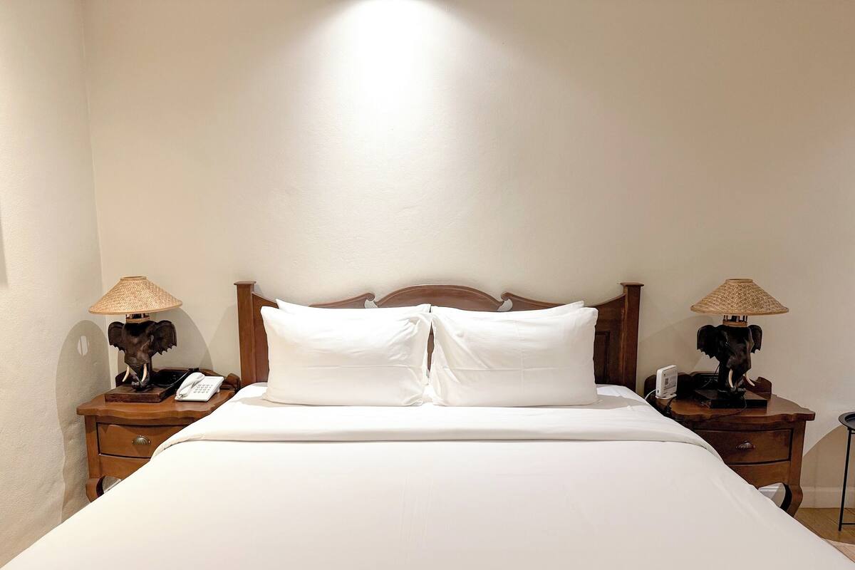 A neatly made bed with white linens and two nightstands with elephant-shaped lamps.