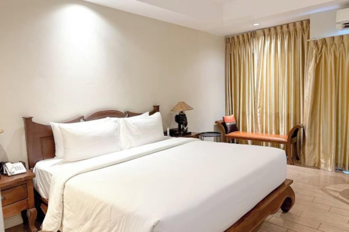 Une chambre d’hôtel avec un grand lit, une table de chevet avec une lampe, une chaise et un rideau.