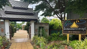 A pathway leading to a building with a traditional roof and a signboard with a contact number. - Kokhaburi Hotel (Ko Kha)