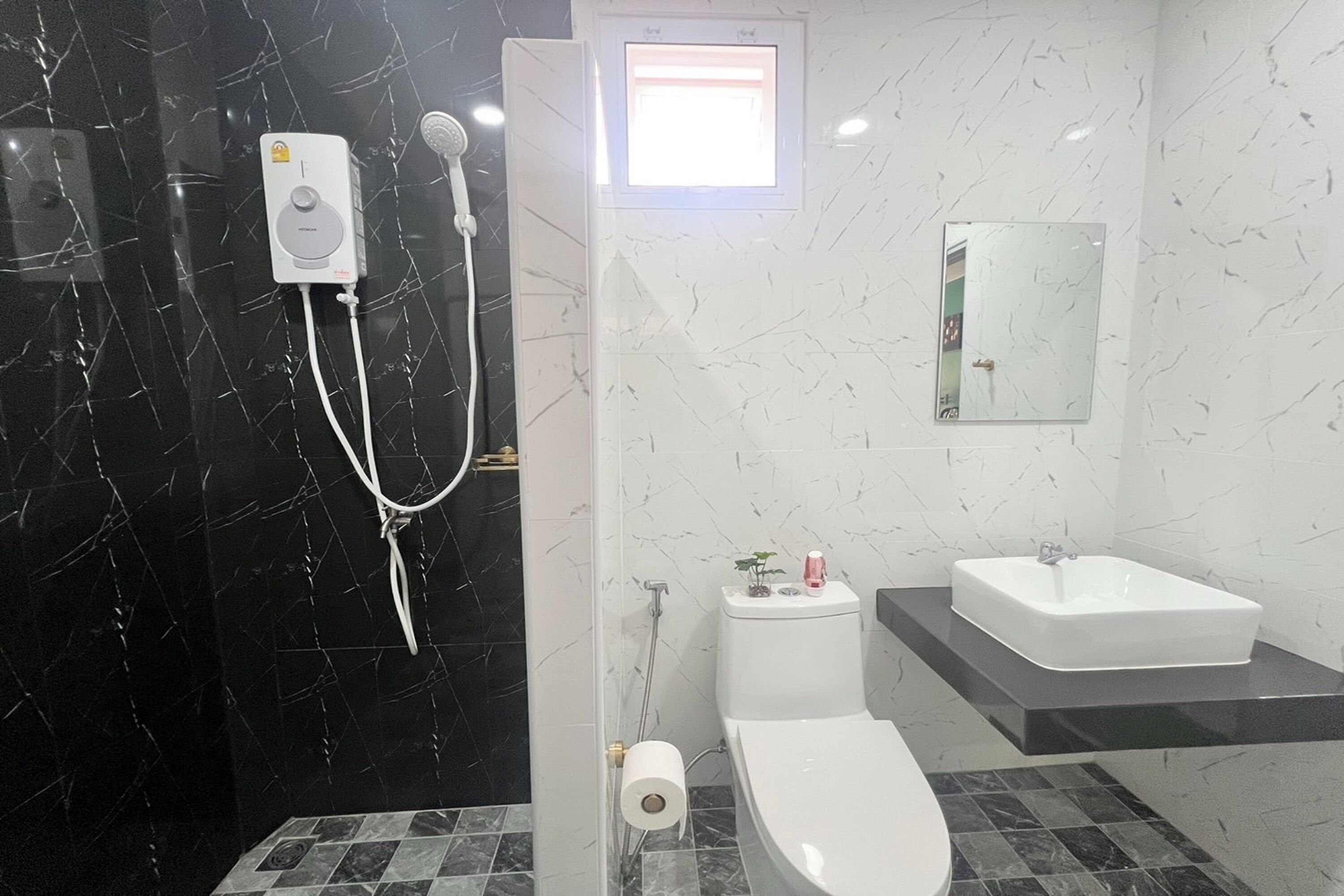A bathroom with a black marble wall, a white toilet, a white sink, and a shower with a handheld showerhead.