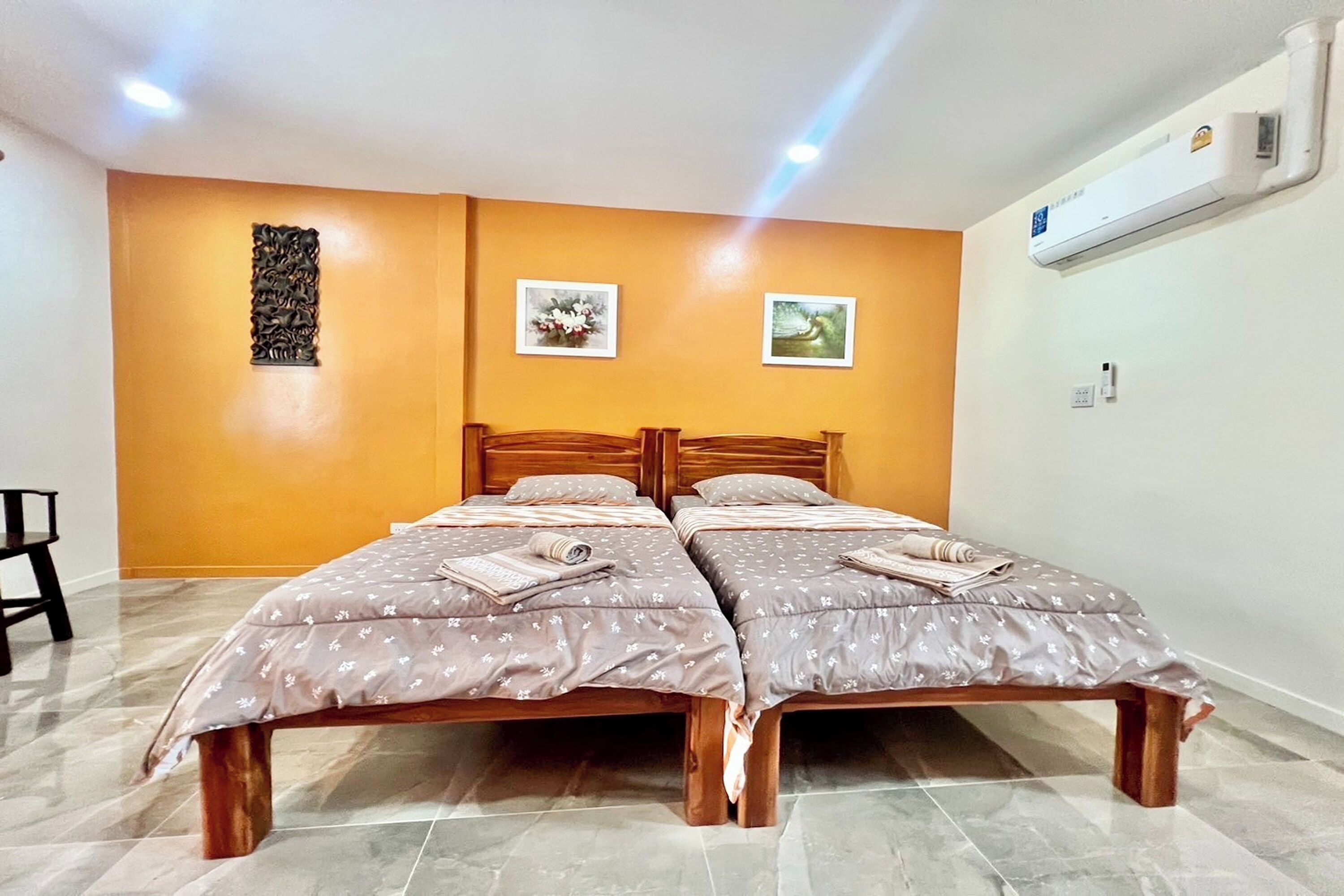 Habitación doble con dos camas, cabecera de madera, aire acondicionado de pared y una pequeña mesa con una silla.