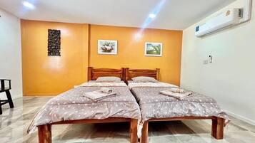 Habitación doble con dos camas, cabecera de madera, aire acondicionado de pared y una pequeña mesa con una silla.