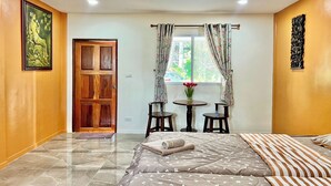 Una habitación de hotel con cama, puerta de madera, una mesita con sillas y una ventana con cortinas.