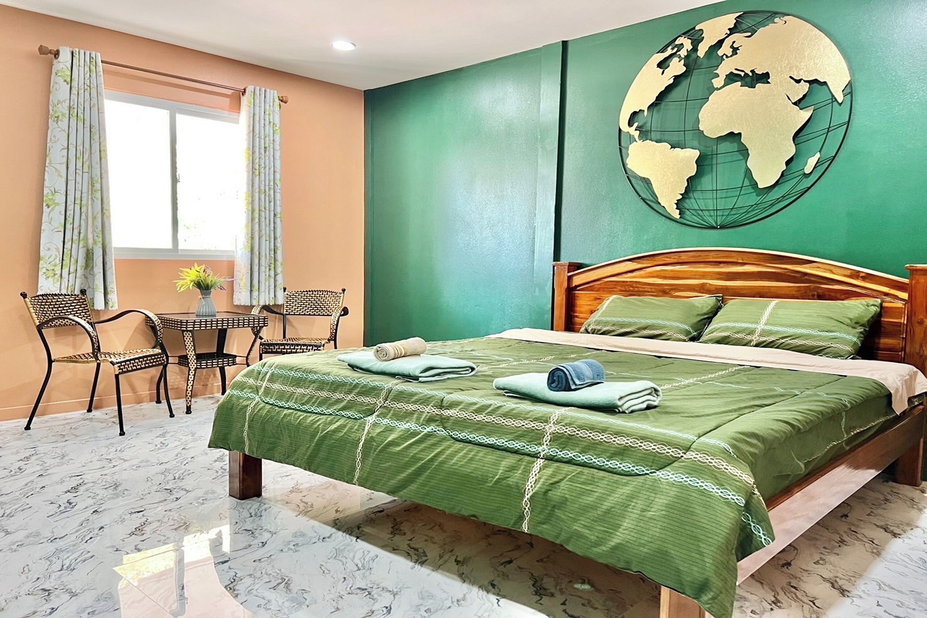 Ein Hotelzimmer mit einem Bett, einem Esstisch mit Stühlen, einem Globus als Wandkunst und einem Fenster mit Vorhängen.