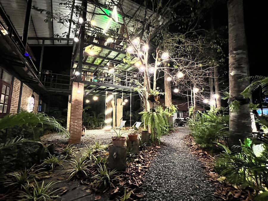 Zona exterior nocturna amb passatge cobert, plantes en testos i camí de grava.