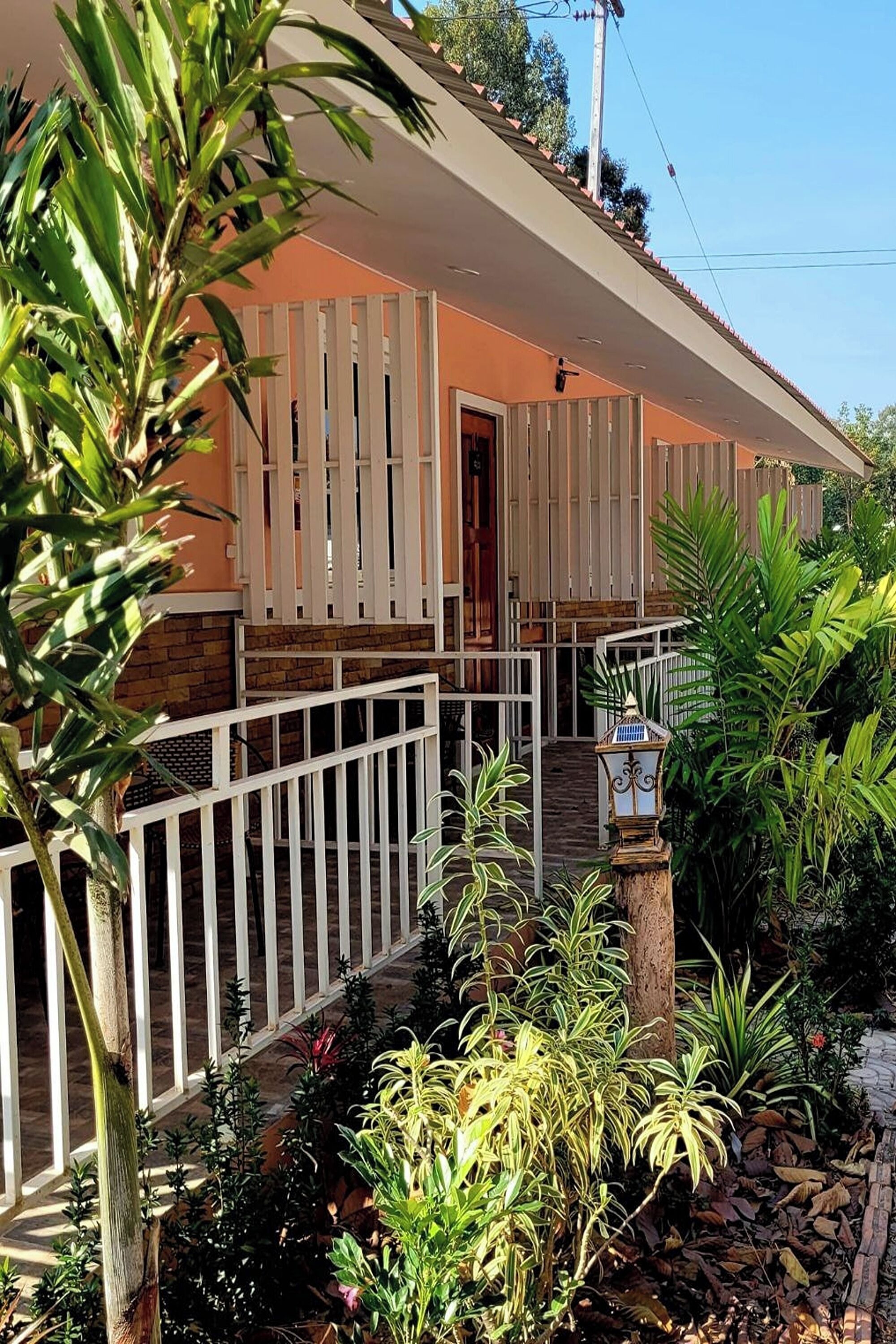 A two-story building with a balcony, surrounded by lush greenery and a stone pathway.