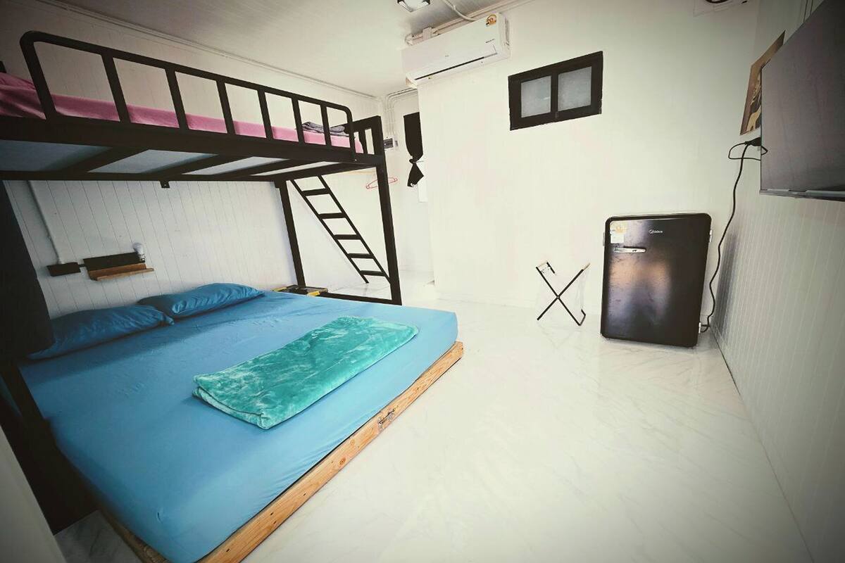 A dorm-style room with bunk beds, a small refrigerator, and a ladder.