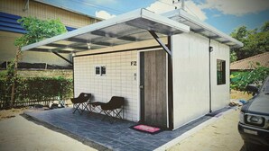 A small, single-story building with a tiled exterior, a covered porch with two chairs, and a car parked outside. - Kua Car Camp (Lampang)