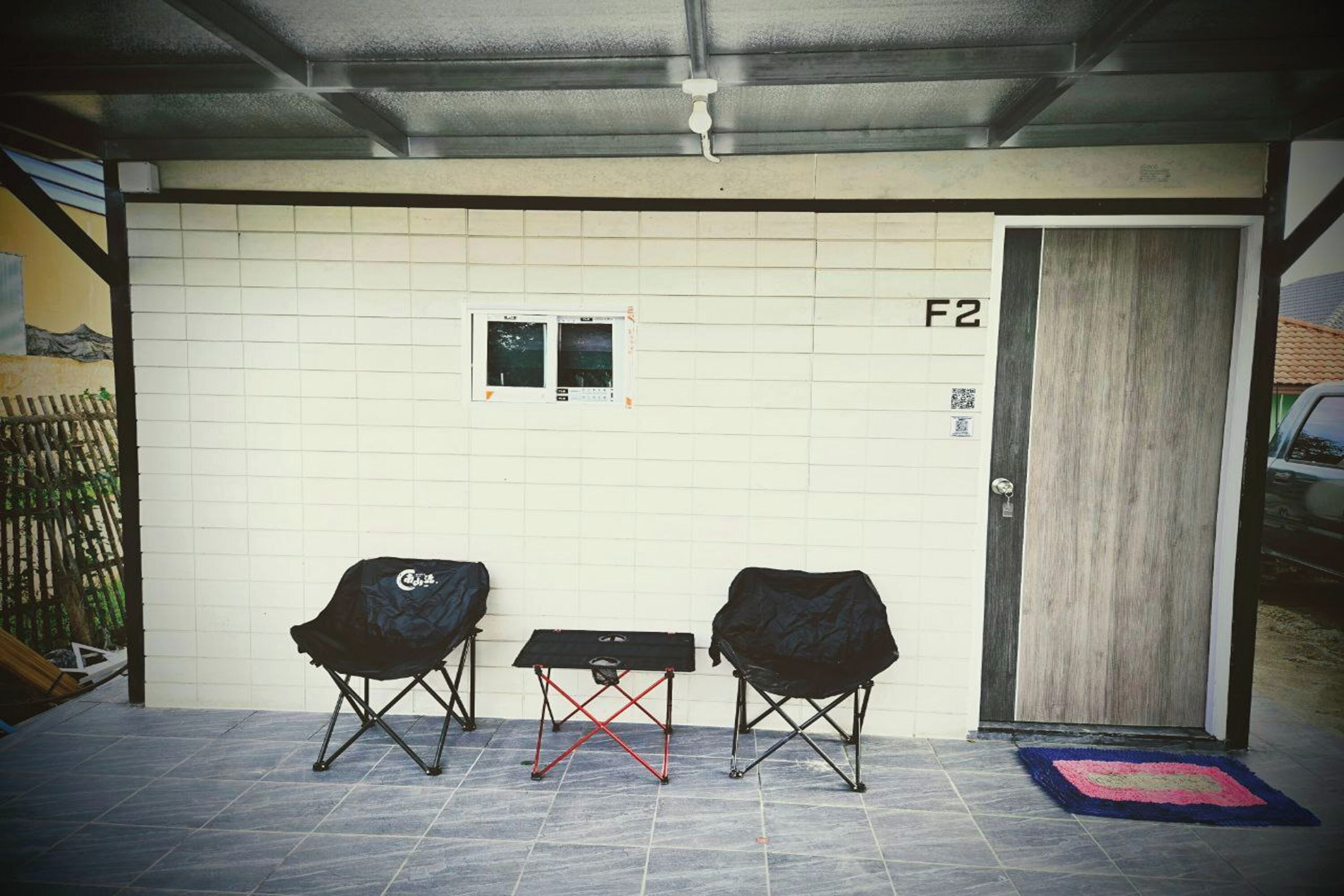 A covered outdoor area with two folding chairs, a small table, and a door marked F2.