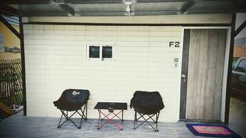 A covered outdoor area with two folding chairs, a small table, and a door marked F2.