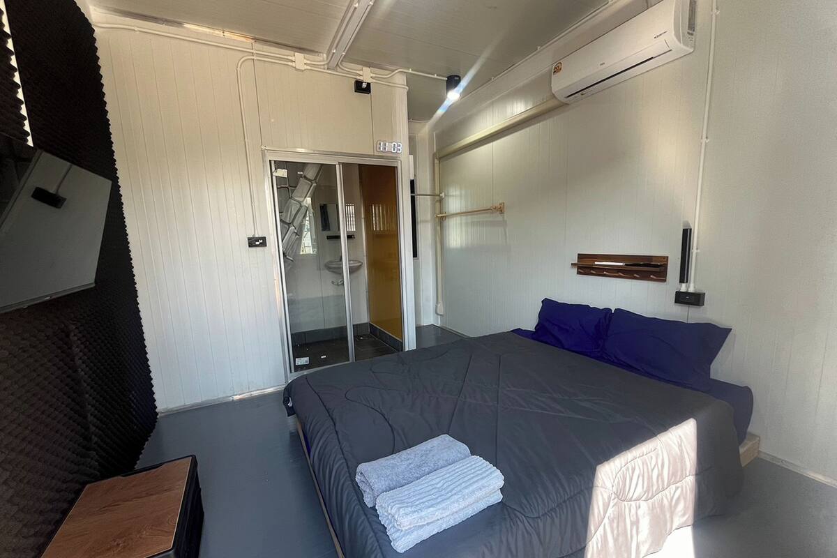 A modern hotel room with a large bed, a small desk, a walk-in closet, and a bathroom with a glass door.