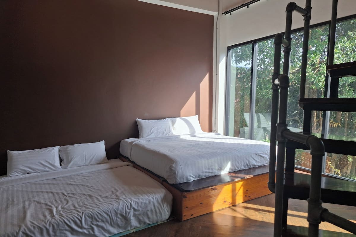 Una habitación con dos camas, un ventanal con vistas a la vegetación y suelo de madera.
