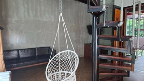 Ein Zimmer mit einer schwarzen Ledersofa, einem weißen Makramee-Hängesessel und einer Holztreppe mit Metallgeländern.