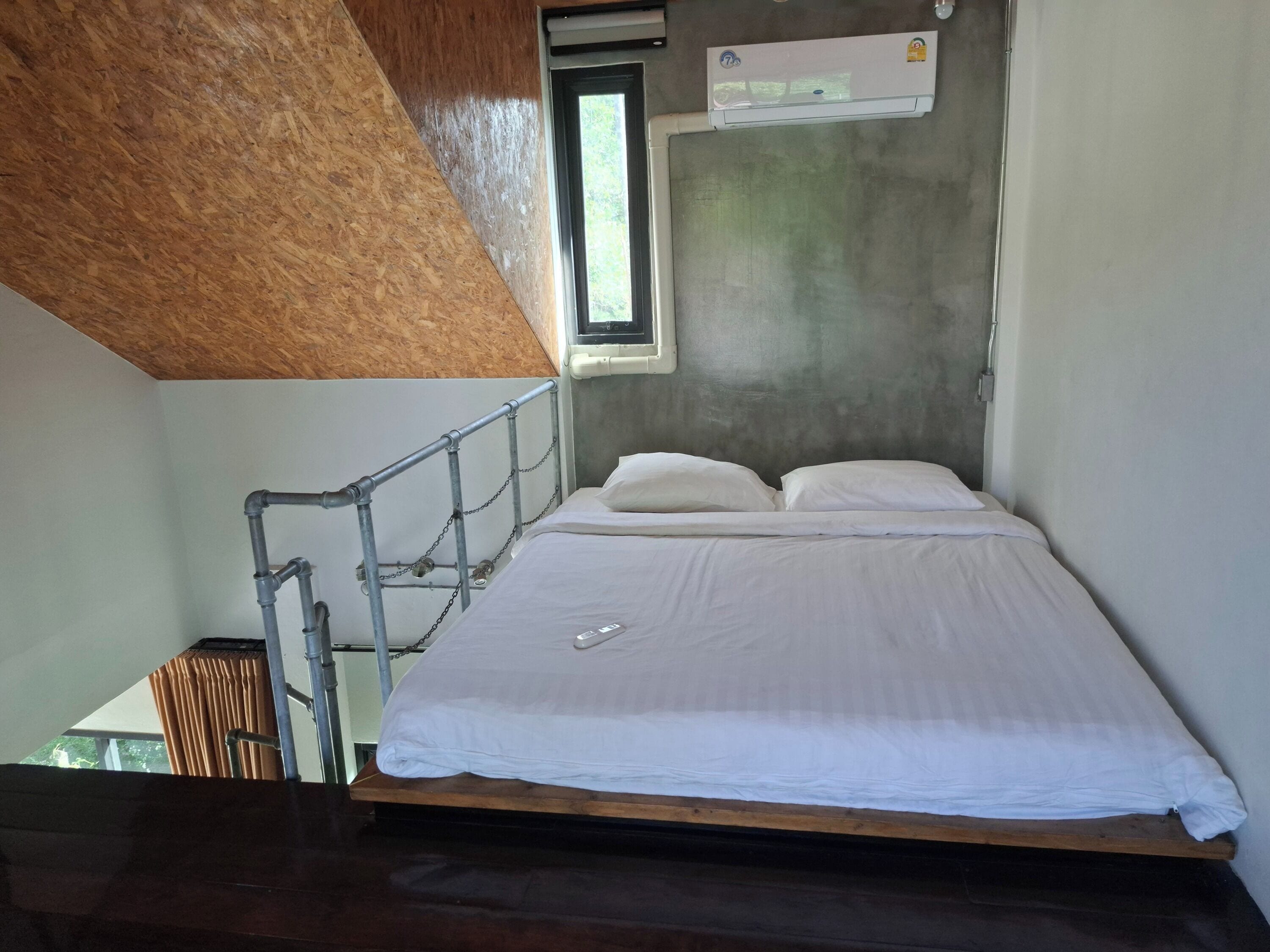 En enkeltseng med hvide sengetøj i et rum med skråvægge og et vindue.