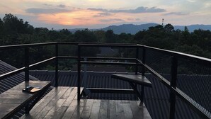 Eine Holzterrasse mit Metallgeländer, die auf einen bewaldeten Bereich mit entfernten Bergen blickt.