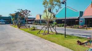 A street with colorful buildings, a swing set, and a palm tree. - Pai Tawan Resort Hotel - Pet friendly (Khon Kaen)