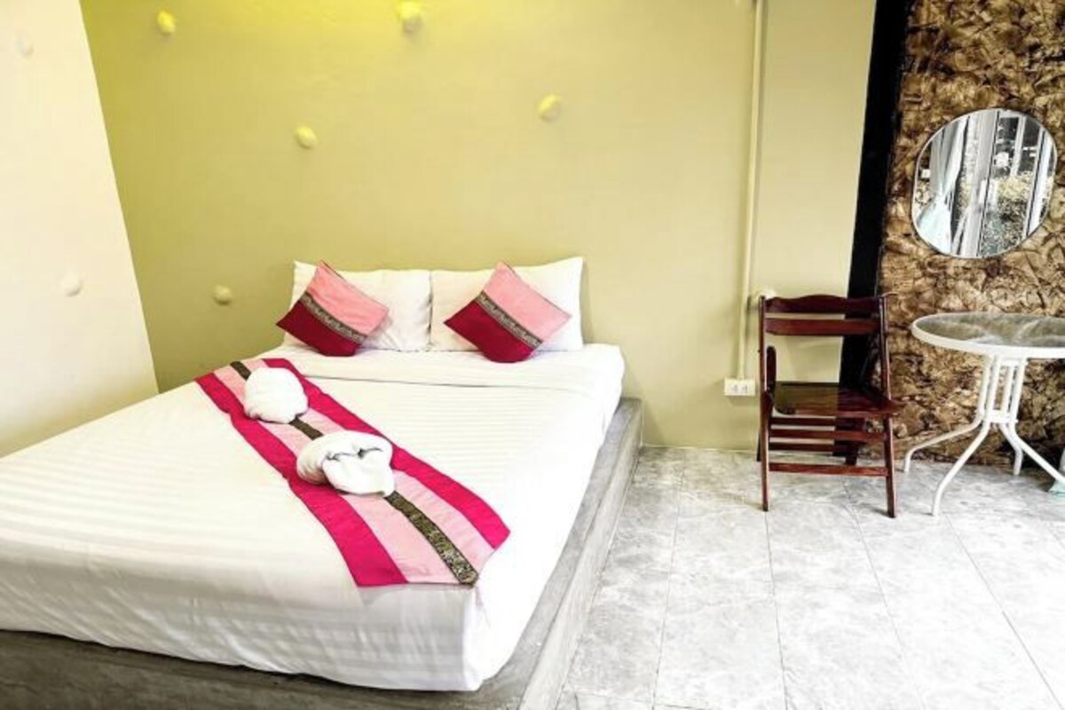Ein Hotelzimmer mit Bett, Kissen, einem Sessel, einem runden Spiegel und einem kleinen Tisch.