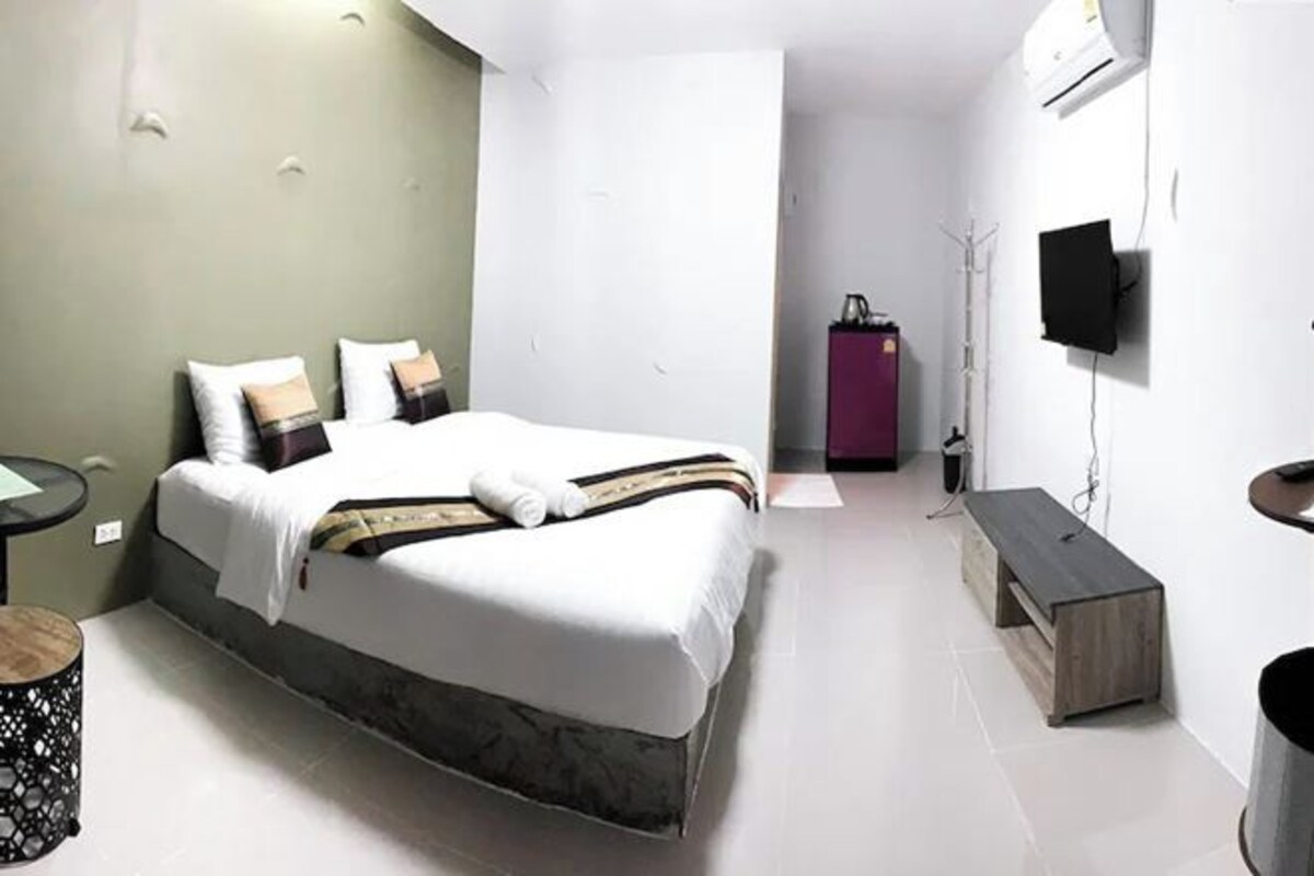 Ein modernes Hotelzimmer mit einem großen Bett, einem kleinen runden Tisch, einer Bank, einem an der Wand befestigten Fernseher und einem Kleiderschrank.