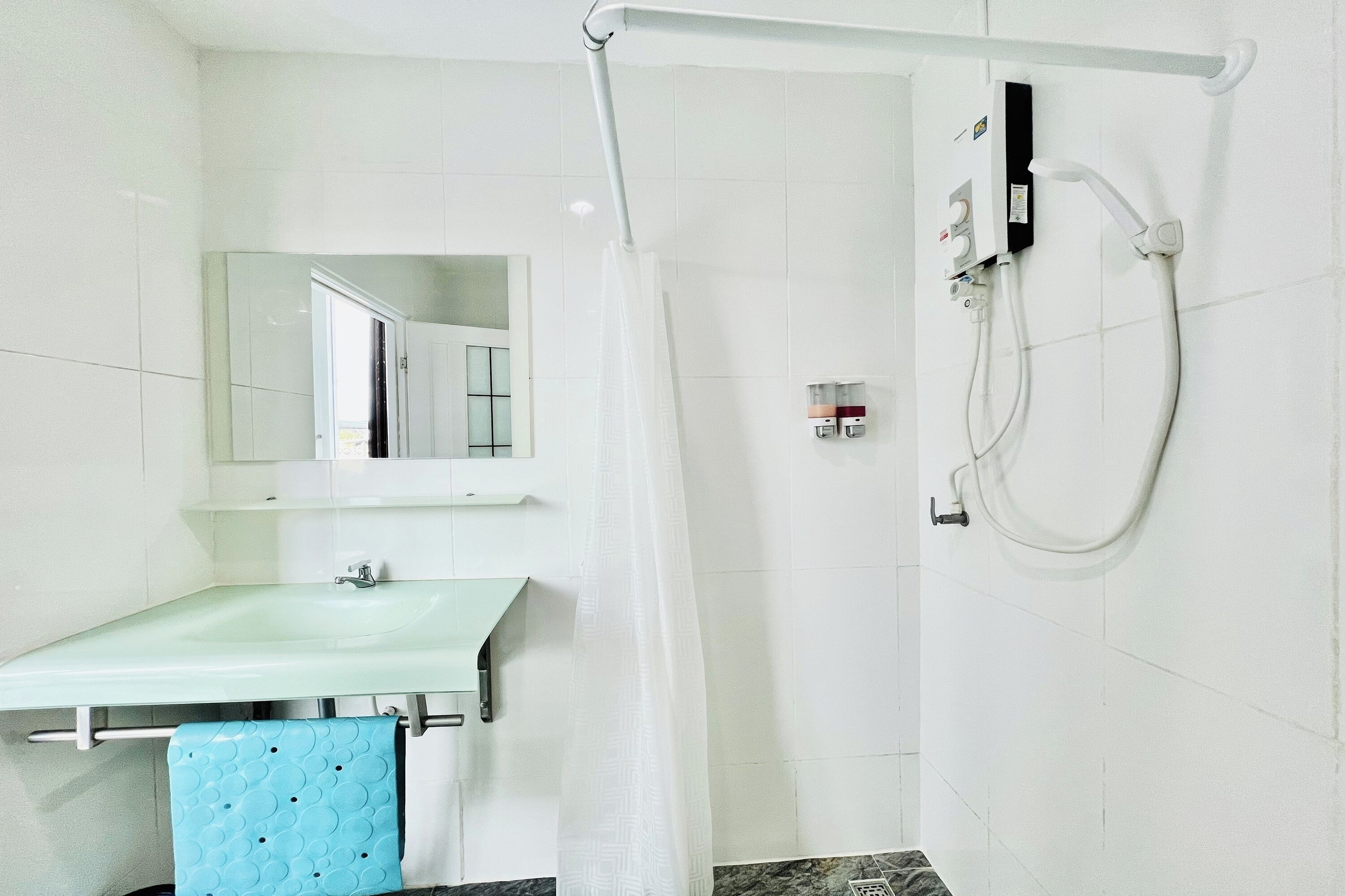 Un baño con un lavamanos blanco, un espejo, una ducha con cabezal de ducha manual y un perchero con una toalla azul.