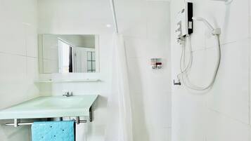Un baño con un lavamanos blanco, un espejo, una ducha con cabezal de ducha manual y un perchero con una toalla azul.