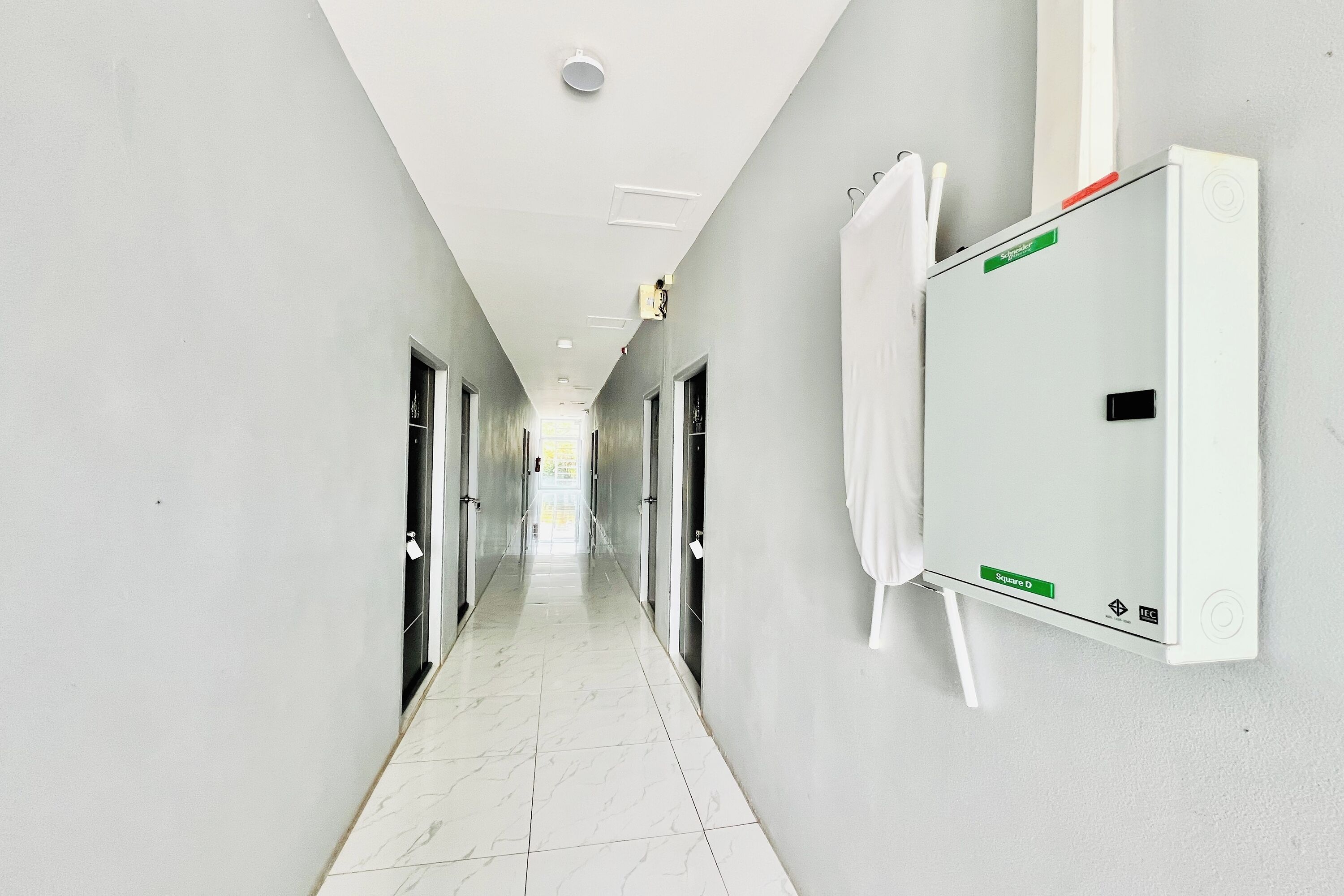A hallway with a white tiled floor, doors on both sides, and a whiteboard on the right wall.