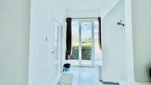 A narrow hallway with a sliding glass door leading to a balcony. A small rug is placed on the floor, and a black trash bin is visible near the door. - Parichat Bandung Hotel (Ban Dung)