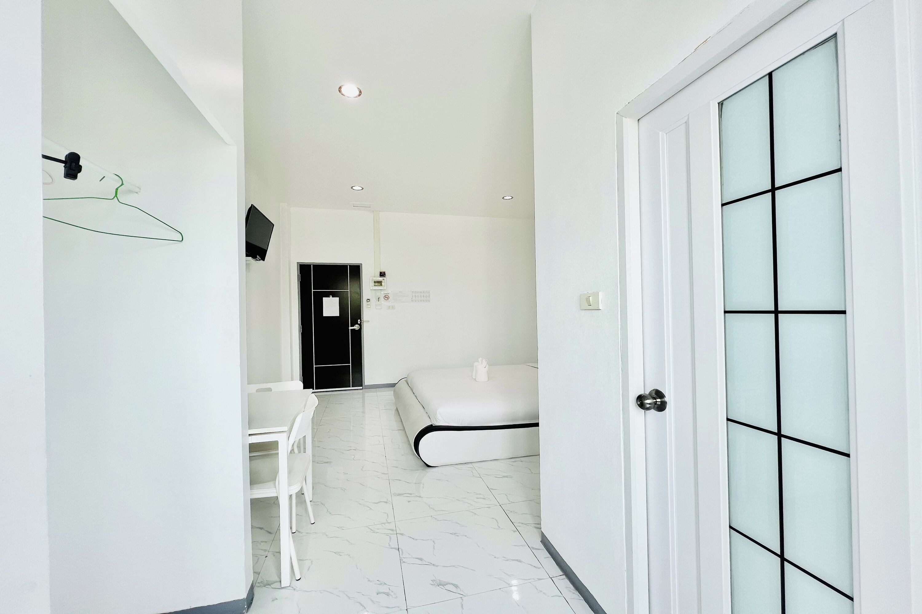 Una habitación de hotel moderna con una cama blanca, un escritorio pequeño, una silla y una puerta con paneles de vidrio esmerilado.