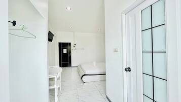 A modern hotel room with a white bed, a small desk, a chair, and a door with frosted glass panels.