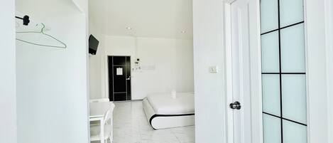 Una habitación de hotel moderna con una cama blanca, un escritorio pequeño, una silla y una puerta con paneles de vidrio esmerilado.