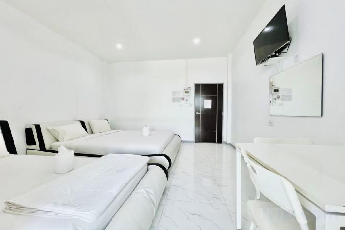 A hotel room with two beds, a desk, a television, and a door.