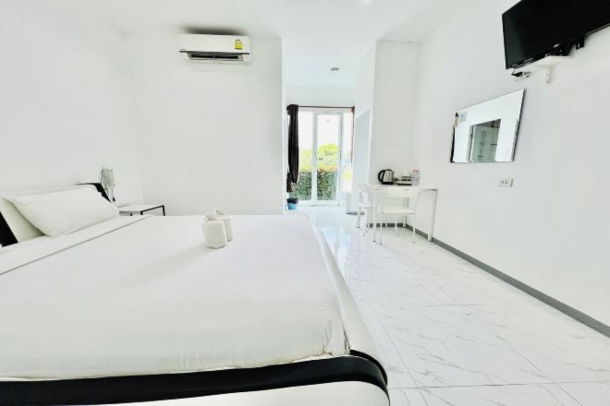 A hotel room with a large bed, a desk, a chair, a mirror, and a TV.