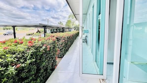 A hotel corridor with a covered walkway, a glass wall, and a row of neatly trimmed hedges. - Parichat Bandung Hotel (Ban Dung)