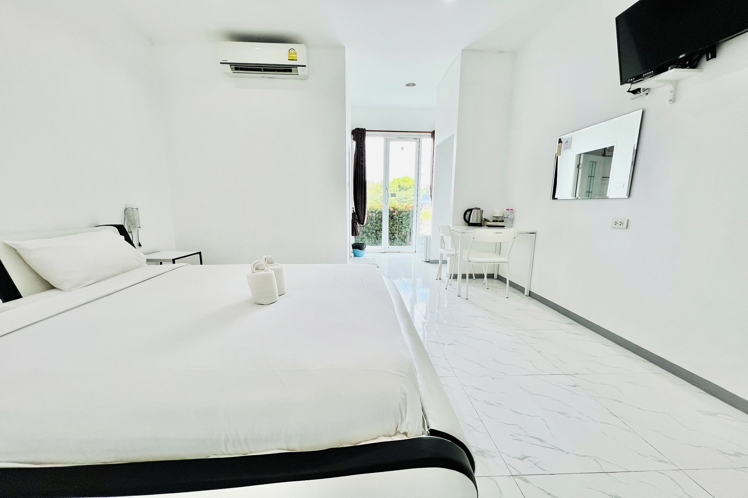 A hotel room with a large bed, a desk, a chair, a TV, and a window with curtains.
