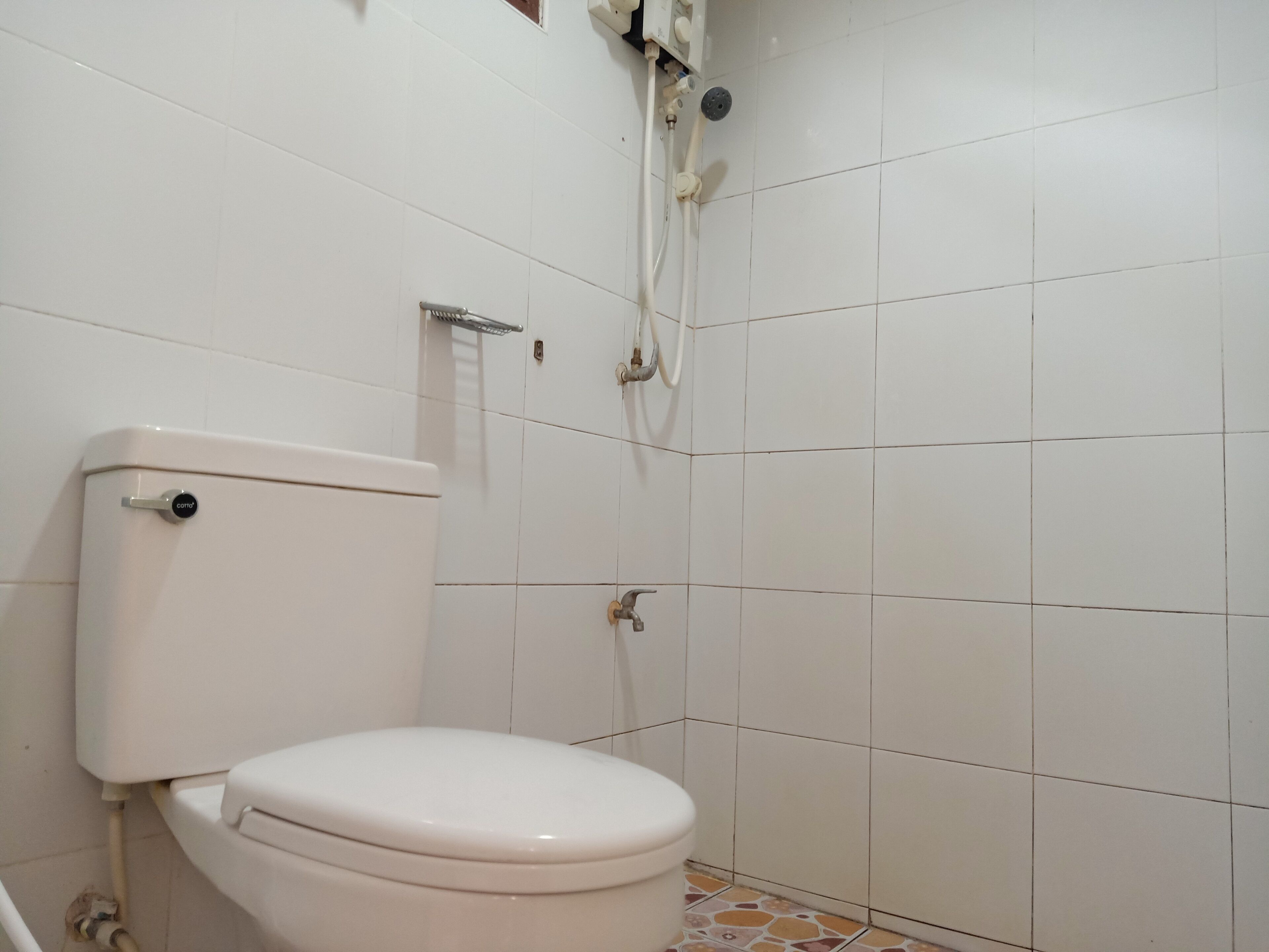 Et standard toilet med tanke, brusehoved og flisegulv.