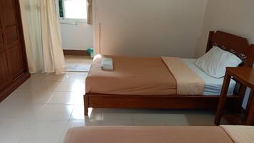 Una habitación con dos camas individuales, cabecera y mesita de noche de madera, una ventana con cortinas y suelo de baldosas.