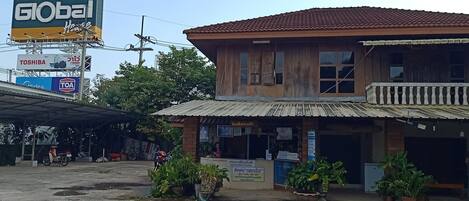 A two-story building with a tiled roof and a balcony. There are potted plants in front of the building.