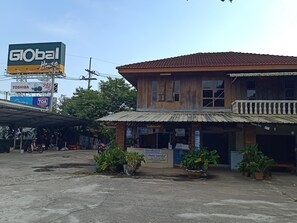 A two-story building with a tiled roof and a balcony. There are potted plants in front of the building. - Phumchan Place Hotel (Phayao)
