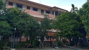 A multi-story building with a tiled roof, surrounded by lush greenery and a bench. - Phumchan Place Hotel (Phayao)