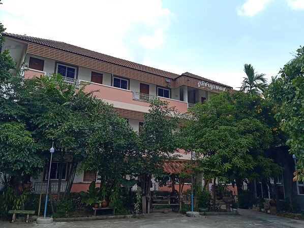 A multi-story building with a tiled roof, surrounded by lush greenery and a bench. - Phumchan Place Hotel (Phayao)