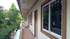 A corridor with a tiled floor, white walls, and large windows with blinds. - Phumchan Place Hotel (Phayao)